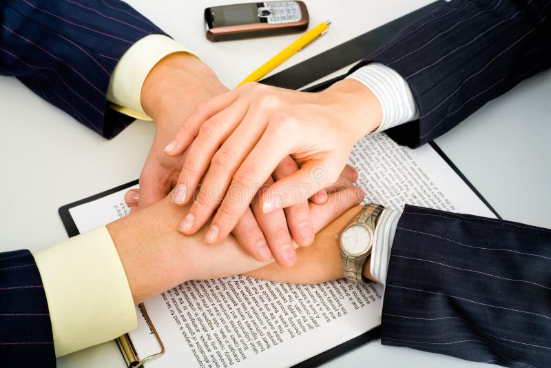 Photo of two business partners holding their hands over the contract lying on the table with a yellow pen, a ruler and a cellular phone near by. Photo of two business partners holding their hands over the contract lying on the table with a yellow pen, a ruler and a cellular phone near by