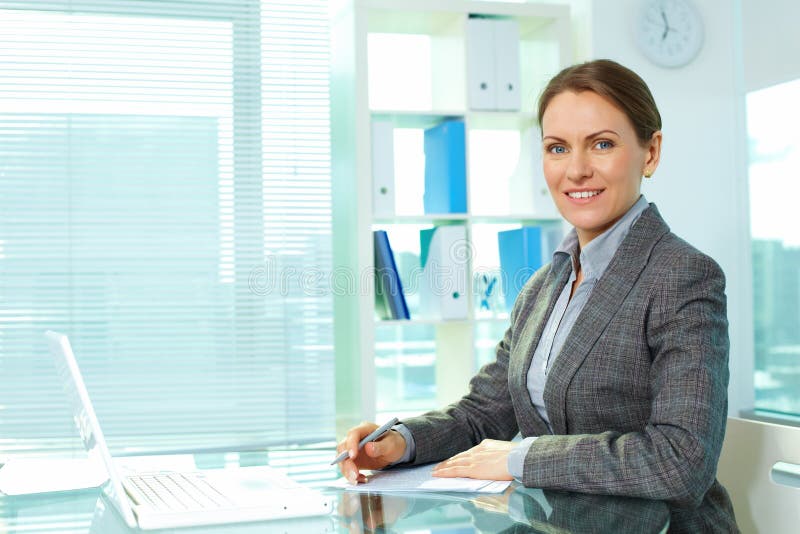 Cheerful business lady smiling at camera sitting at her workplace. Cheerful business lady smiling at camera sitting at her workplace