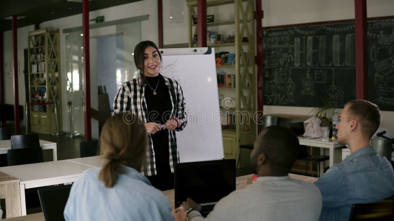 Bedrijfsmensen bij seminariezitting in een modern bureau Jong mooi brunette in plaidoverhemd die bevinden zich dichtbij whiteboar