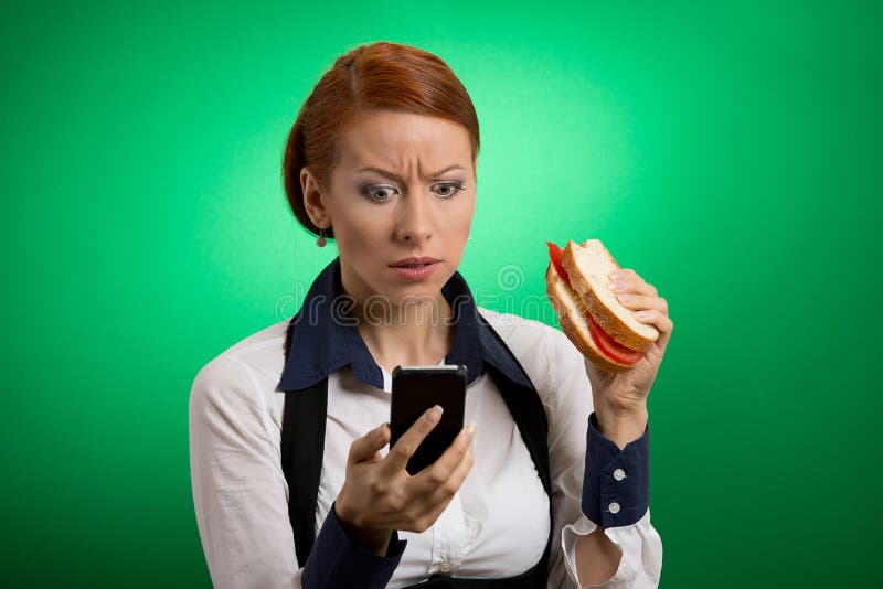 Bedrijfsvrouw die mobiele telefoon bekijken die sandwich eten royalty-vrije stock afbeelding Bedrijfsvrouw die mobiele telefoon bekijken die sandwich eten royalty-vrije stock afbeelding