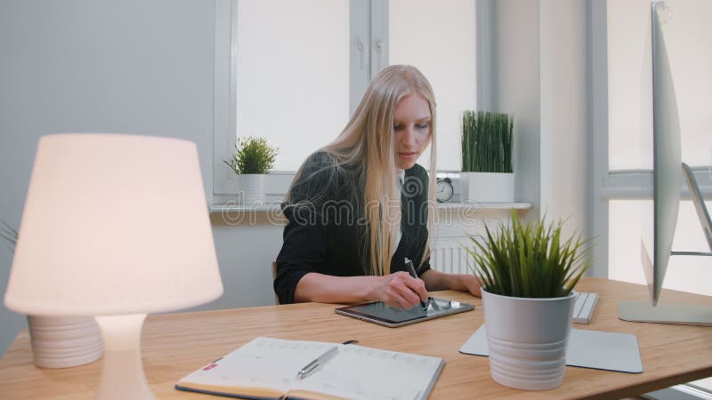 Bedrijfsvrouwen die aan tablet in bureau werken Aantrekkelijk blond wijfje met lang haar in elegante kostuumzitting bij houten