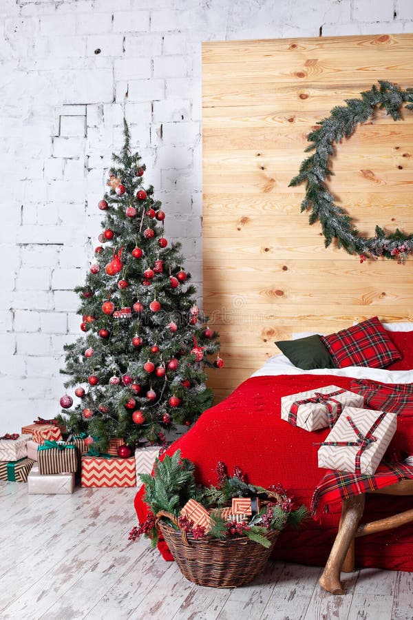 Bedroom is decorated for Christmas. Cozy bright room: red plaid, a wooden bed and basket with gifts. In room is a Christmas tree d