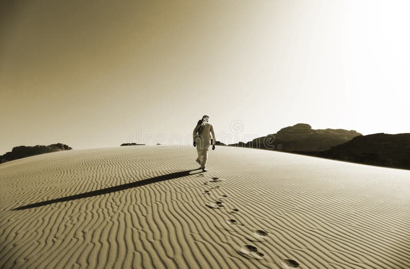 Beduino che cammina sulle dune di sabbia in Wadi Rum Desert, Giordania nel colore di seppia fotografie stock libere da diritti Beduino che cammina sulle dune di sabbia in Wadi Rum Desert, Giordania nel colore di seppia fotografie stock libere da diritti