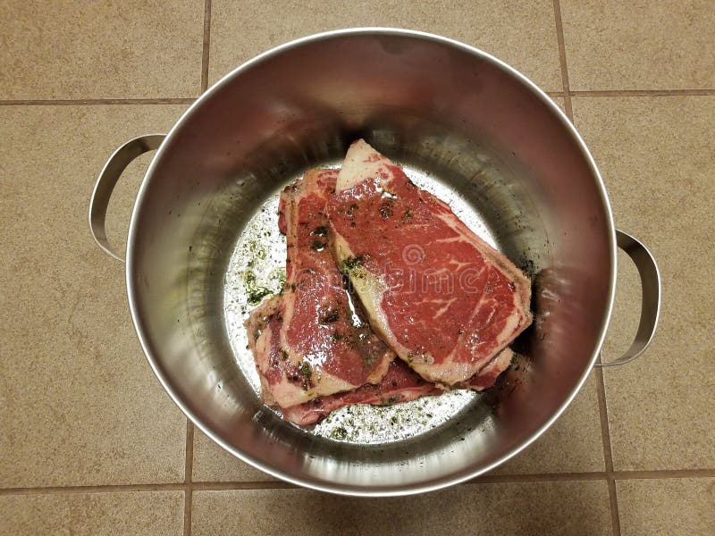 Beef Steak with Seasoning and Liquid in Metal Pot on Tile Floor Stock