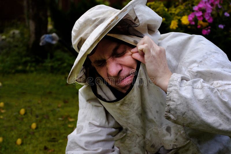 A beekeeper with a painful face got a bee bite, a garden in the background. A beekeeper with a painful face got a bee bite, a garden in the background