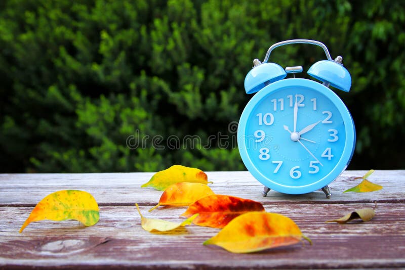 Beeld van de Verandering van de de herfsttijd Dalings achterconcept Droog bladeren en uitstekende Wekker in openlucht op houten l stock fotografie Beeld van de Verandering van de de herfsttijd Dalings achterconcept Droog bladeren en uitstekende Wekker in openlucht op houten l stock fotografie