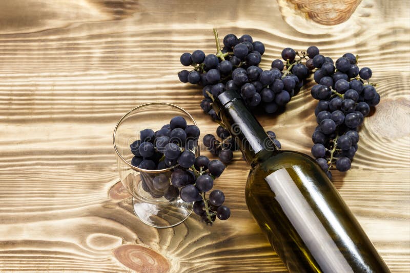 Beeld van een glas, vers geplukte ontbroken verwerking, zwarte druiven op een houten achtergrond en een lege fles stock foto Beeld van een glas, vers geplukte ontbroken verwerking, zwarte druiven op een houten achtergrond en een lege fles stock foto