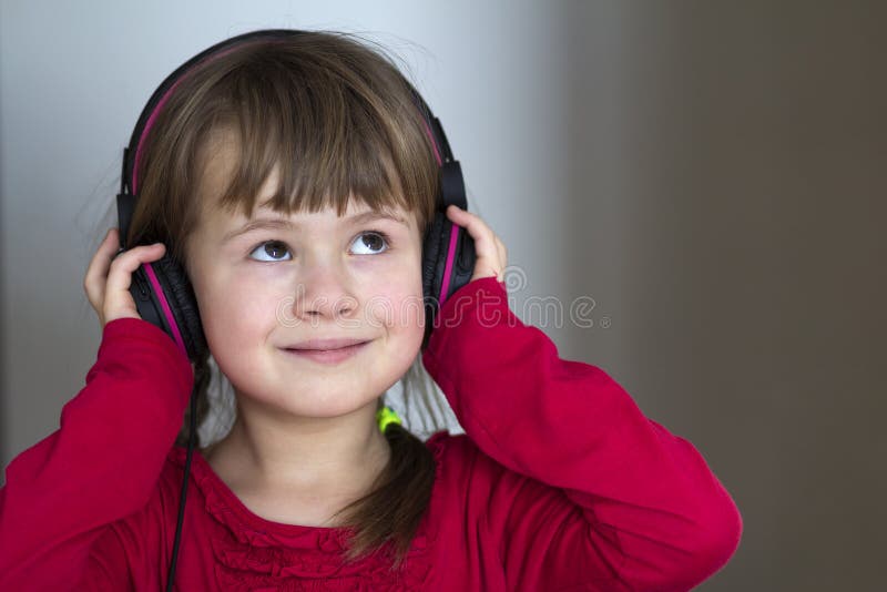 Beeld van gelukkig mooi kindmeisje met grote hoofdtelefoons thuis Blij kindmeisje die aan vage muziek op grijs luisteren backgr stock foto's Beeld van gelukkig mooi kindmeisje met grote hoofdtelefoons thuis Blij kindmeisje die aan vage muziek op grijs luisteren backgr stock foto's