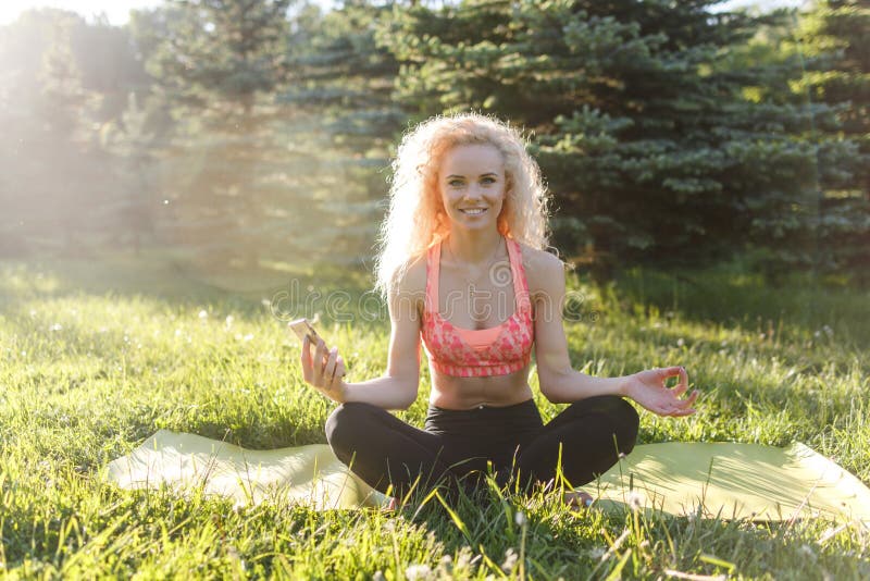 Beeld van jonge krullend-haired sportenvrouw het praktizeren yoga op deken in park royalty-vrije stock fotografie Beeld van jonge krullend-haired sportenvrouw het praktizeren yoga op deken in park royalty-vrije stock fotografie
