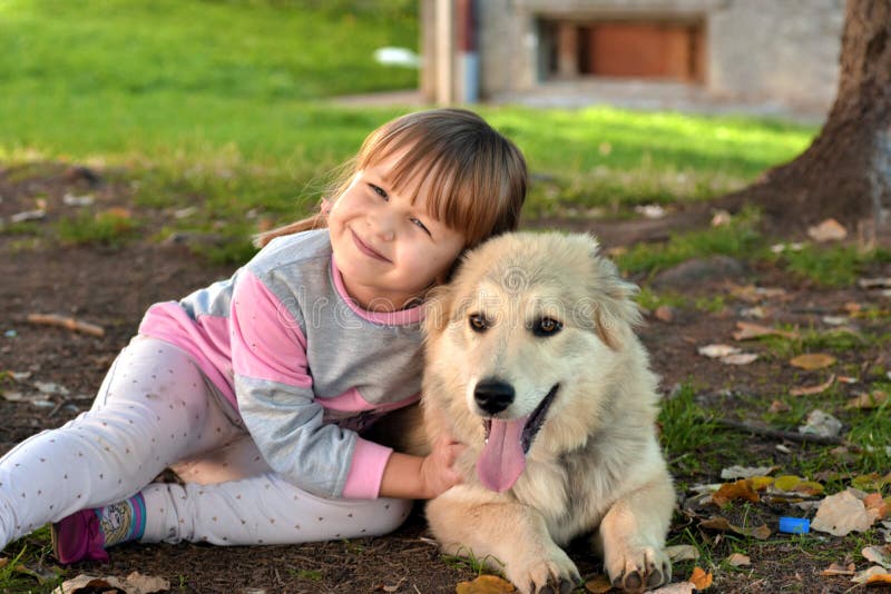 Beeld van meisje die witte puppyhond koesteren die op parkgrond leggen stock afbeeldingen Beeld van meisje die witte puppyhond koesteren die op parkgrond leggen stock afbeeldingen