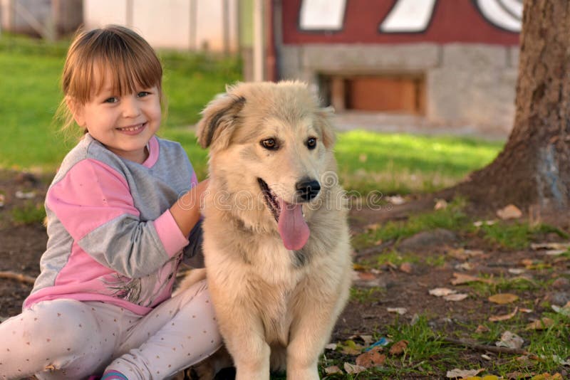 Beeld van meisje die witte puppyhond koesteren die op parkgrond leggen royalty-vrije stock fotografie Beeld van meisje die witte puppyhond koesteren die op parkgrond leggen royalty-vrije stock fotografie