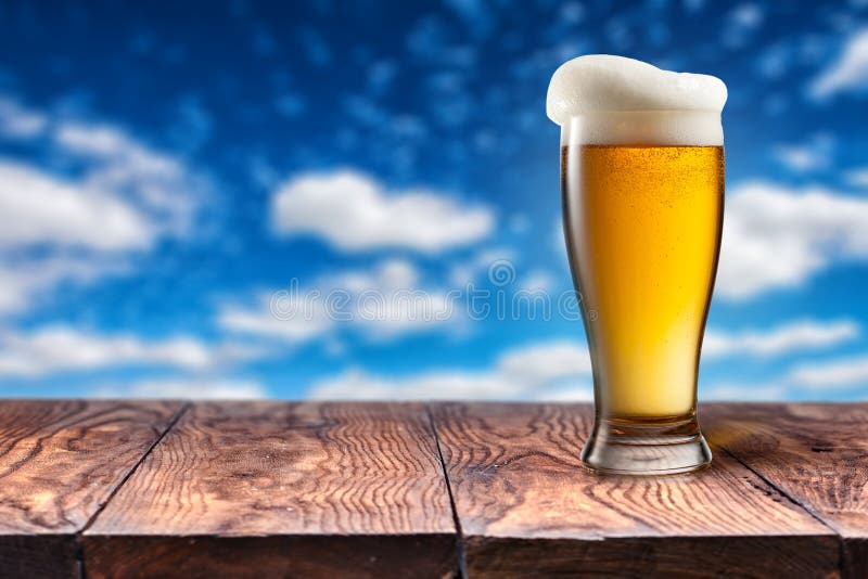 Beer in glass on wooden table against blue sky