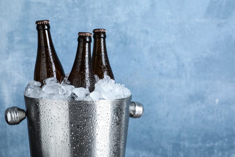 Beer in metal bucket with ice on blue background, closeup. Space for text