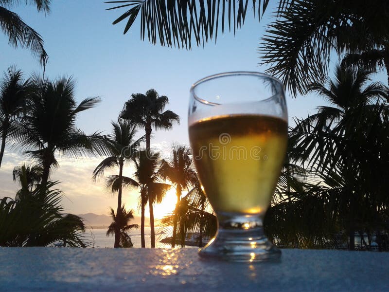 A glass of beer with palm trees in silhouette at sunset. Las Hadas Resort in Manzanillo, Colima, Mexico. A glass of beer with palm trees in silhouette at sunset. Las Hadas Resort in Manzanillo, Colima, Mexico.