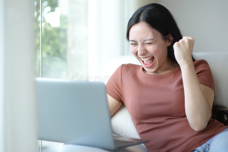 Begeisterte Asiatin, die zu Hause Laptop benutzt lizenzfreie stockbilder