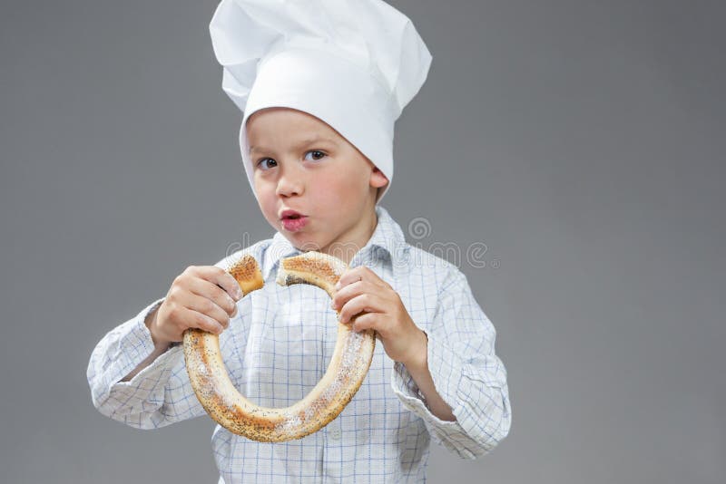 Begeisterter Kaukasier Little Boy, das neues Donut-Brötchen isst Aufstellung, wenn Hut gekocht wird stockbild Begeisterter Kaukasier Little Boy, das neues Donut-Brötchen isst Aufstellung, wenn Hut gekocht wird stockbild