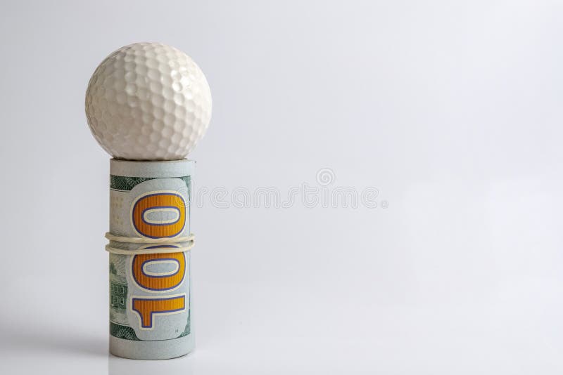 Concept of financial risk or golfer competition for money or sports betting or corruption. A roll of American hundred dollar bills tied with a white rubber band with a golf ball on top. Concept of financial risk or golfer competition for money or sports betting or corruption. A roll of American hundred dollar bills tied with a white rubber band with a golf ball on top