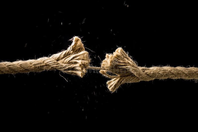 Concept of danger and risk with two ends of a frayed worn rope held together by the last strand on the point of snapping, against a dark background with copyspace. Concept of danger and risk with two ends of a frayed worn rope held together by the last strand on the point of snapping, against a dark background with copyspace.