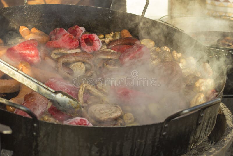Begreppet av gatamat: grönsaker och korvar grillar, ånga över en stekpanna, suddighet arkivbilder Begreppet av gatamat: grönsaker och korvar grillar, ånga över en stekpanna, suddighet arkivbilder