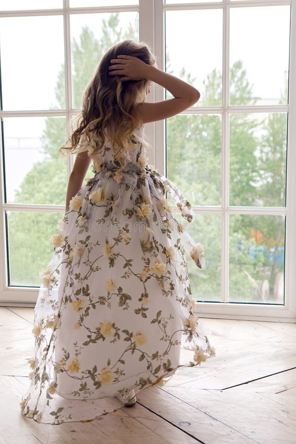 Behandla som ett barn flickan i långa ställningar för en blom- klänning royaltyfri foto Behandla som ett barn flickan i långa ställningar för en blom- klänning royaltyfri foto