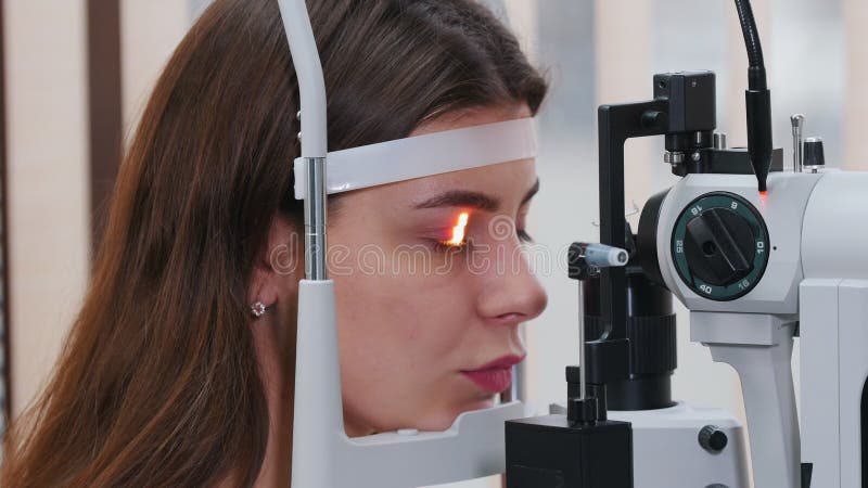 Behandling av ögonsjukdomar - en ung kvinna som kontrollerar synskärpan med ett ljus av en speciell stor optometrisk maskin stock video
