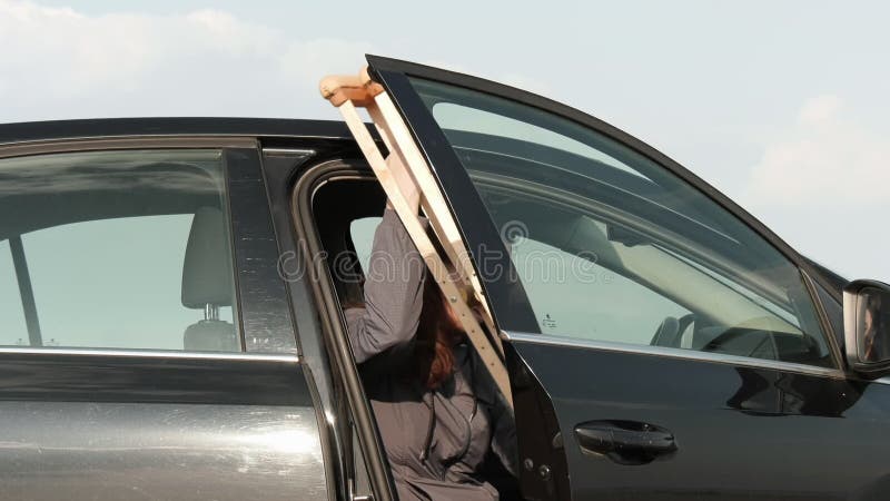 Behinderte mit Krücken versuchen, in das Auto zu kommen. mit einem Sicherheitsgurt befestigt