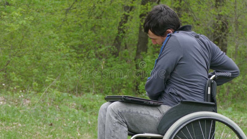 Behinderter Mann denkt müdes an Bruchproblemrollstuhl mit Laptop beim Arbeiten an Naturgrünhintergrund
