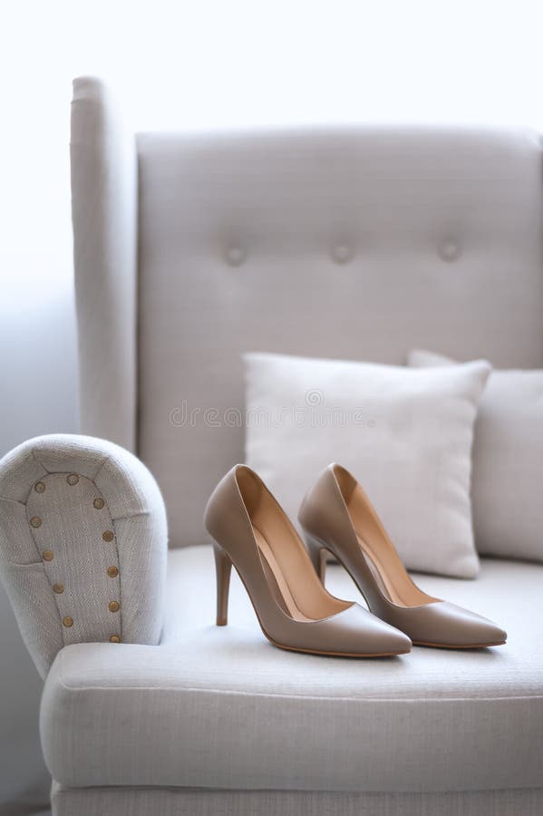 Beige wedding shoes on white sofa close up. Luxury pair of highheel female shoes on a couch