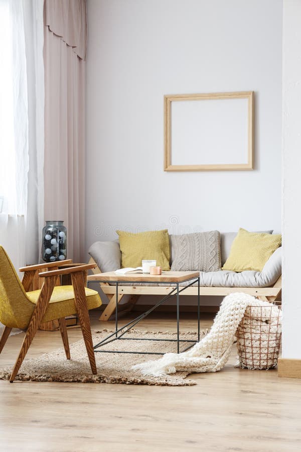 Beige and yellow interior decor of modern bright living room with sofa, wooden furniture and frame decoration on the white wall. Beige and yellow interior decor of modern bright living room with sofa, wooden furniture and frame decoration on the white wall