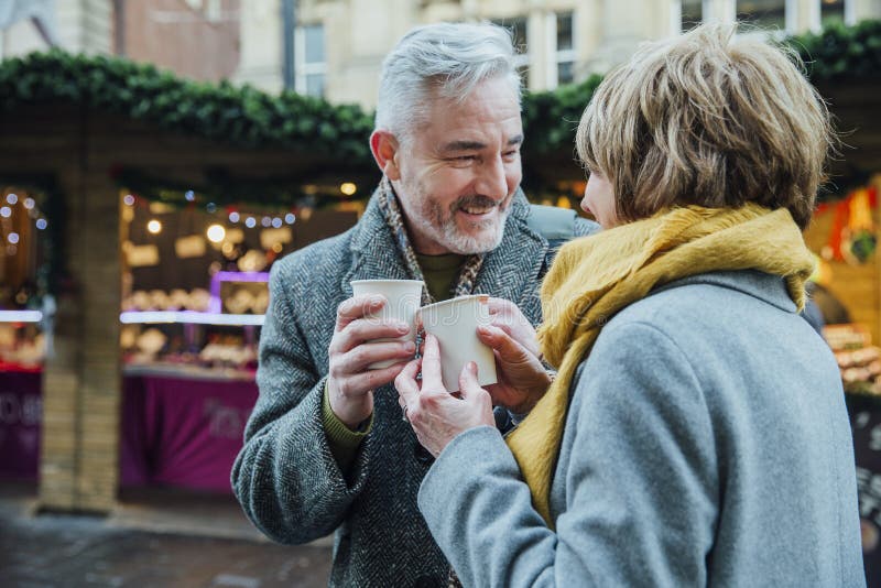 Mature couple are drinking hot drinks in a town christmas market. They are toasting the disposable cups. Mature couple are drinking hot drinks in a town christmas market. They are toasting the disposable cups.