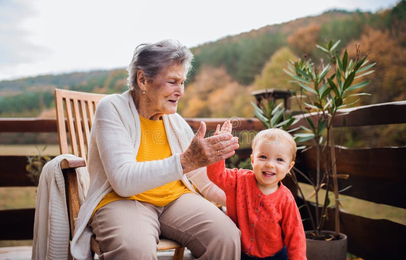 Bejaarde met een peuter groot-kleinkind op een terras in herfst, die hoogte vijf de geven stock afbeeldingen Bejaarde met een peuter groot-kleinkind op een terras in herfst, die hoogte vijf de geven stock afbeeldingen