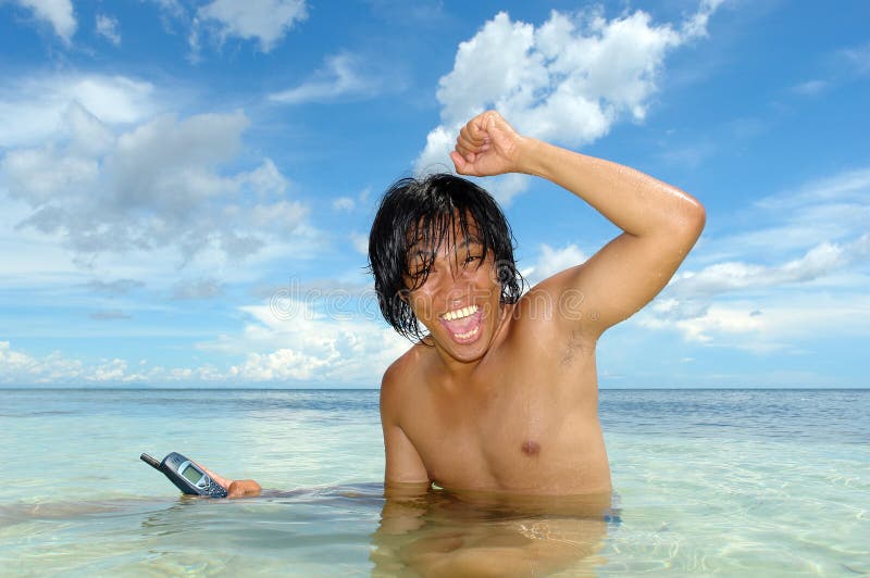 Bekanntmachen eines Cell-phone in einem tropischen Meer durch einen asiatischen Jungen. lizenzfreie stockfotografie Bekanntmachen eines Cell-phone in einem tropischen Meer durch einen asiatischen Jungen. lizenzfreie stockfotografie