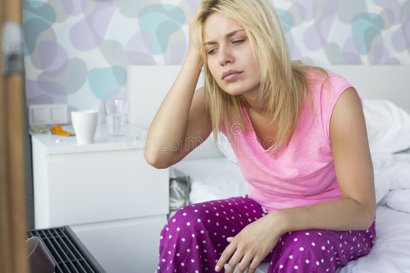 Beklemtoonde vrouw die aan hoofdpijnzitting thuis lijden op bed stock fotografie Beklemtoonde vrouw die aan hoofdpijnzitting thuis lijden op bed stock fotografie