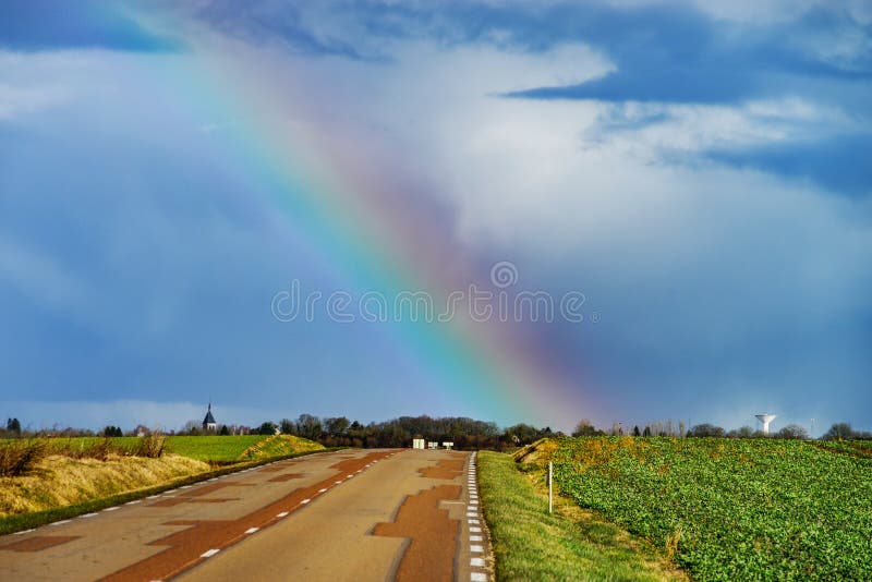 Bel arc-en-ciel coloré à l'extrémité de la route goudronnée, perspecti photo stock Bel arc-en-ciel coloré à l'extrémité de la route goudronnée, perspecti photo stock