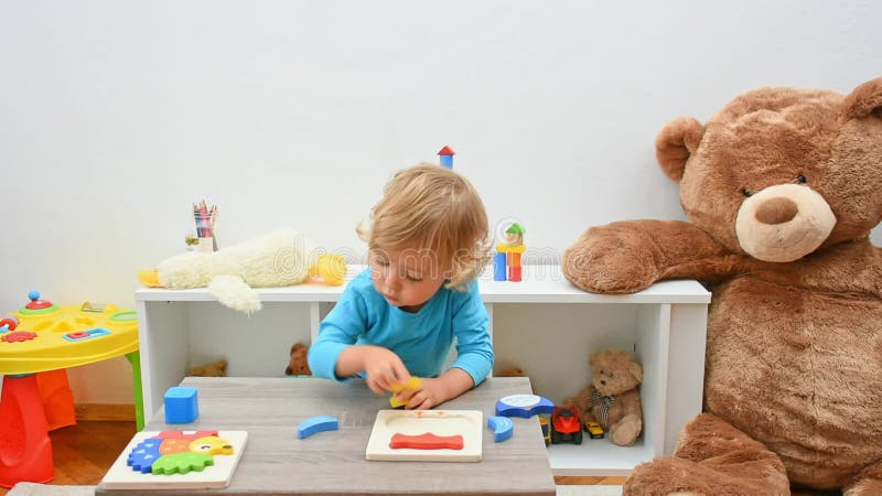 Bel bambino felice che si diverte a giocare con un puzzle di legno colorato a casa. attività interna per bambini archivi video