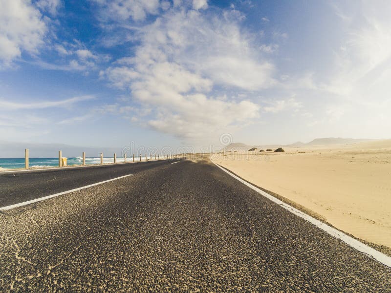 Bela estrada cênica com dunas de areia desértica e praia com água do oceano azul nos lados - céu azul com nuvens no fundo - imagem de stock Bela estrada cênica com dunas de areia desértica e praia com água do oceano azul nos lados - céu azul com nuvens no fundo - imagem de stock