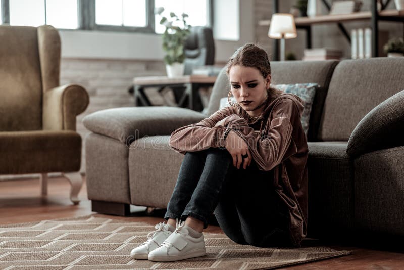 Belastade bärande vita gymnastikskor för den tonårs- flickan som sitter på golvkänslan royaltyfri fotografi Belastade bärande vita gymnastikskor för den tonårs- flickan som sitter på golvkänslan royaltyfri fotografi