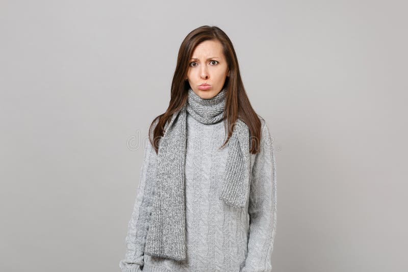 Beledigde jonge vrouw in grijze die sweater, sjaal het pruilen lippen op grijze muurachtergrond worden geïsoleerd, studioportret stock afbeelding Beledigde jonge vrouw in grijze die sweater, sjaal het pruilen lippen op grijze muurachtergrond worden geïsoleerd, studioportret stock afbeelding