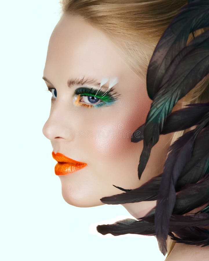 Beautiful woman with artistic gold and orange lips and green eyelashes with feathers on light background. Beautiful woman with artistic gold and orange lips and green eyelashes with feathers on light background