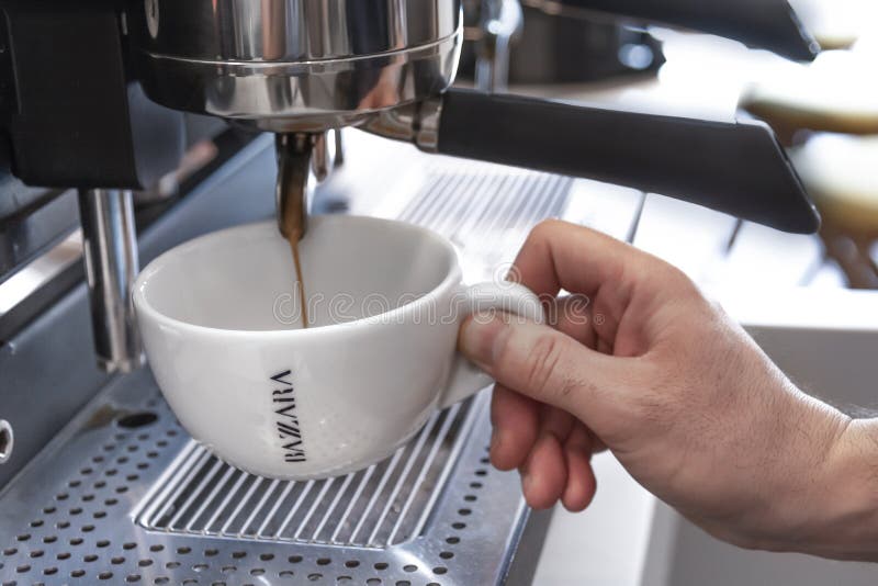 BELGRADE, SERBIE - 10 MARS 2018 main d'homme tenant la tasse de Bazzara versant de la machine d'expresso Belgrade Serbie image libre de droits BELGRADE, SERBIE - 10 MARS 2018 main d'homme tenant la tasse de Bazzara versant de la machine d'expresso Belgrade Serbie image libre de droits