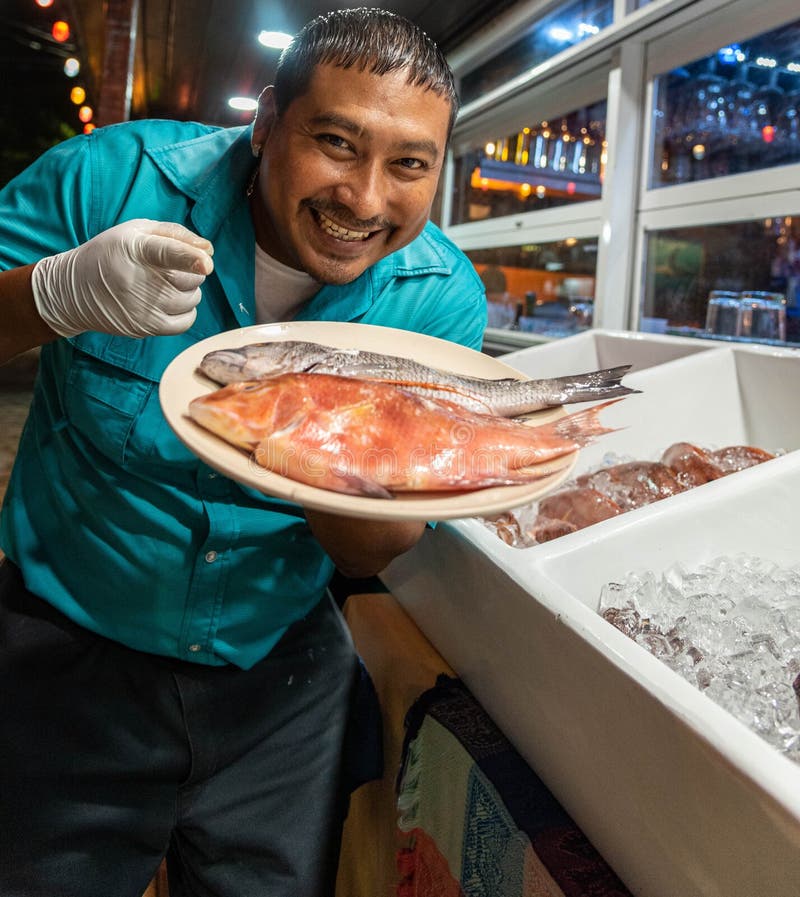 A Belizean restaurant employee is displaying a plate of fresh fish.