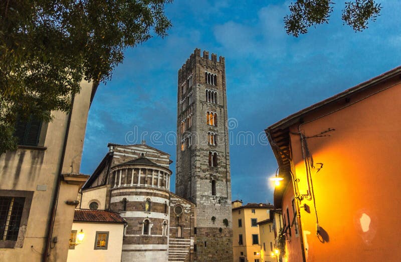 Bell tower of Chiesa di San Frediano catholic church and building with street lamp light on Piazza del Collegio square in historic