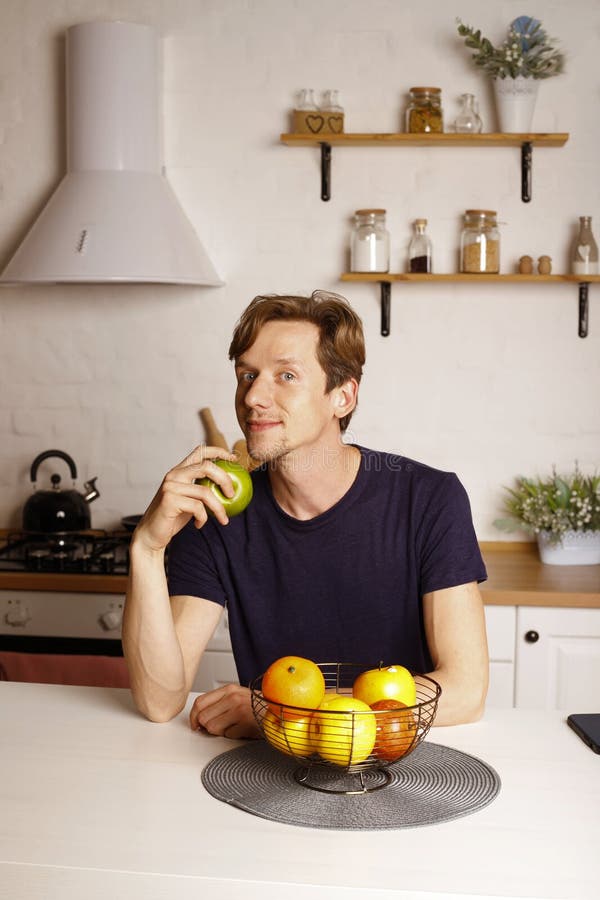Bell'uomo attivo e sano si sente felice quando mangia la mela. giovani e attraenti che mangiano alimenti sani in cucina a casa. be fotografia stock libera da diritti