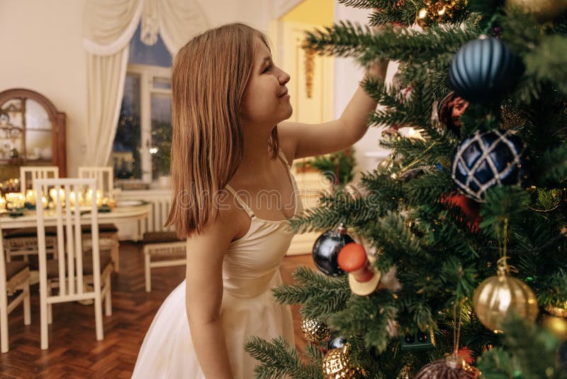 Bella adolescente in abito bianco sta decorando un albero di Natale. una bella ragazza sorride e appende giocattoli di vetro su un immagine stock