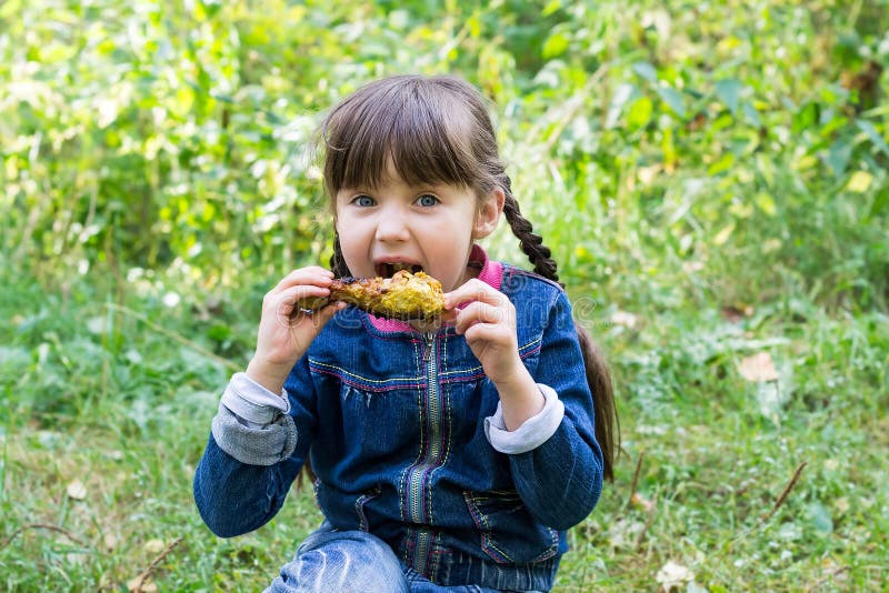 Bella bambina al picnic che mangia una coscia di pollo immagine stock Bella bambina al picnic che mangia una coscia di pollo immagine stock
