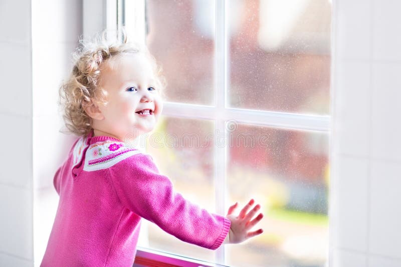 Bella bambina che guarda da una finestra immagine stock Bella bambina che guarda da una finestra immagine stock