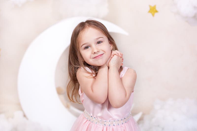 Bella bambina nello studio su un fondo della luna, delle stelle e delle nuvole La bambina sta sognando Sogni dolci cute fotografia stock Bella bambina nello studio su un fondo della luna, delle stelle e delle nuvole La bambina sta sognando Sogni dolci cute fotografia stock