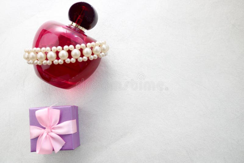 Bella bottiglia trasparente di vetro rosa di profumo femminile decorata con le perle preziose bianche e piccoli contenitore di re immagini stock libere da diritti Bella bottiglia trasparente di vetro rosa di profumo femminile decorata con le perle preziose bianche e piccoli contenitore di re immagini stock libere da diritti