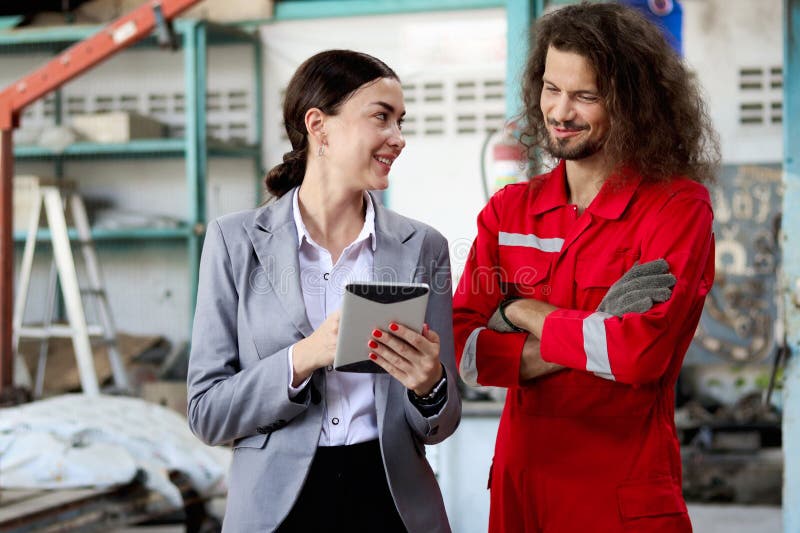 Bella clienta mujer sostiene tableta digital discutiendo con mecánico de uniforme rojo trabajador automotor inspeccionando el auto imágenes de archivo libres de regalías