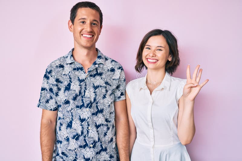 Bella coppia che indossa vestiti casuali che si esibiscono e puntano con le dita numero quattro mentre sorride sicura e felice fotografia stock